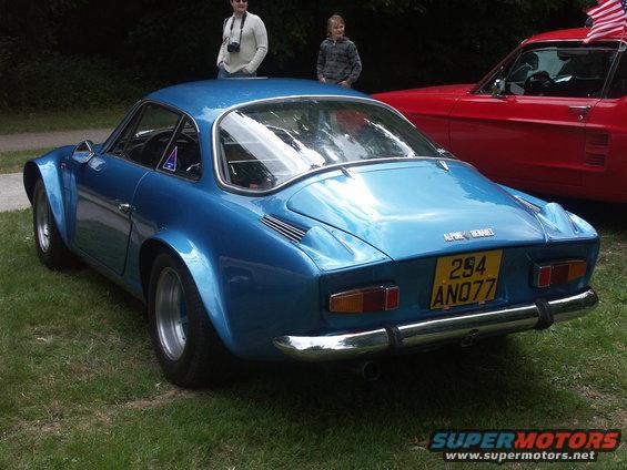 Blue Alpine-Renault coupe, rear view. Yellow license plate reads 294 AN077. Red car visible to the right