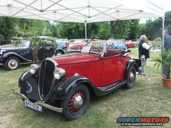 Red convertible vintage car with black fenders and a French license plate AH-916-DF parked on grass under a tent