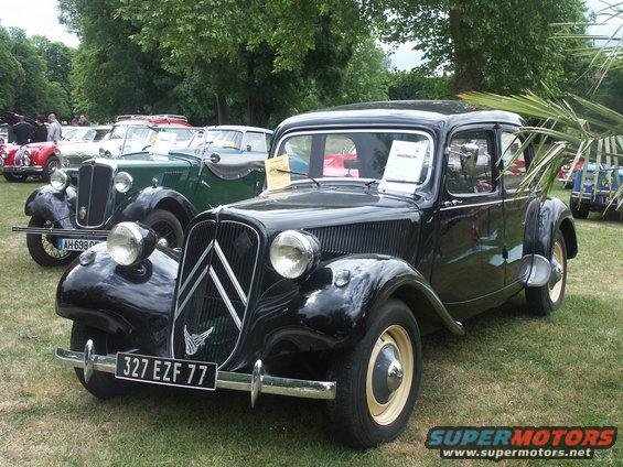 Black Citroën Traction Avant with license plate 327 EZF 77 parked on grass, other vintage cars behind it