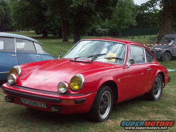 Red Porsche 911 with yellow fog lights and a license plate reading 912OND77. Another blue car is to the left, and a grey Citroen 2CV is in the background