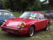 1977 Pontiac Trans Am - A red Porsche 911 is parked on grass with other vehicles in the background.