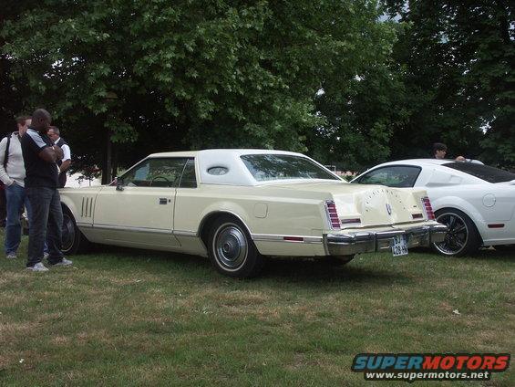 Cream-colored 1977 Lincoln Continental Mark V coupe with a white vinyl roof, seen from the rear 3/4 angle