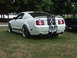 1977 Pontiac Trans Am - White 2005 Ford Mustang GT with black stripes and custom wheels sits on a grassy lawn next to another vehicle.