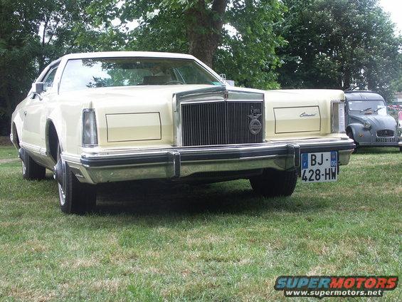 Front view of a cream-colored Lincoln Continental Mark V parked on grass with a grey Citroen 2CV behind it