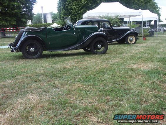 Green convertible and black sedan parked on grass with tents in background