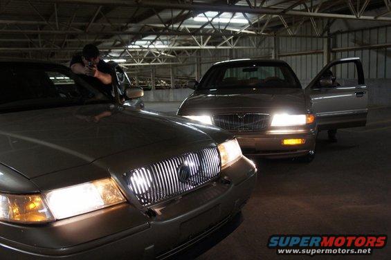 Two tan 2000 Mercury Grand Marquis sedans parked in a garage, one with its driver's door open