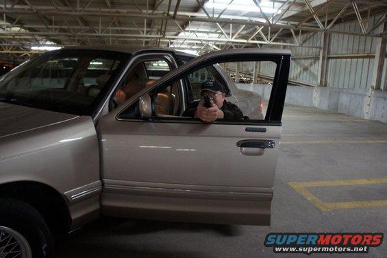 Tan 2000 Mercury Grand Marquis with driver aiming handgun, driver's door open, interior visible