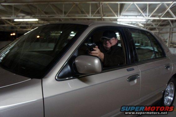 Man in a tan 2000 Mercury Grand Marquis holding a handgun