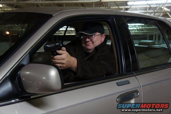Man in a tan 2000 Mercury Grand Marquis holding a handgun, side view