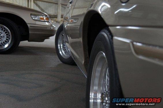Close-up of the side of a tan sedan, with another tan sedan visible behind it. Both have wire-spoke wheels