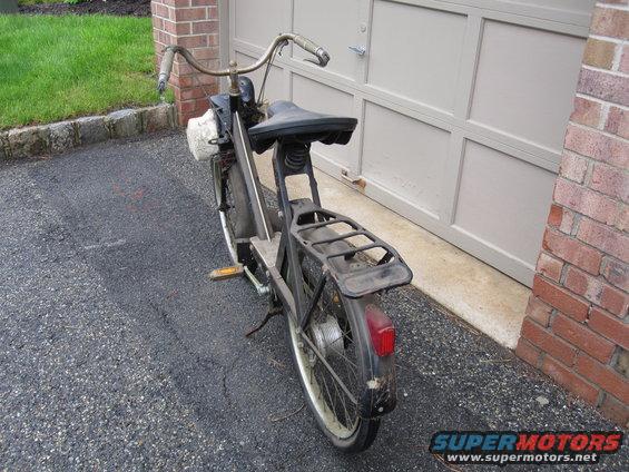 Rear view of a black moped parked on asphalt in front of a garage door