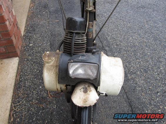 White moped with black engine and headlight assembly, viewed from front. Dirt and grime are visible