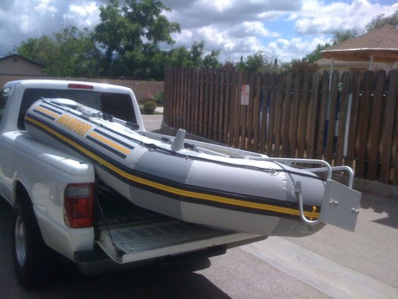 White pickup truck bed carrying a gray inflatable boat with yellow stripes and the word MARINER in yellow