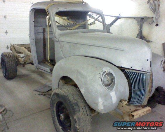 Unfinished 1940 Ford truck body, primer gray, with front grille and fenders visible