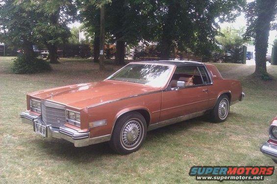 Brown coupe with black vinyl roof parked on grass, front 3/4 view
