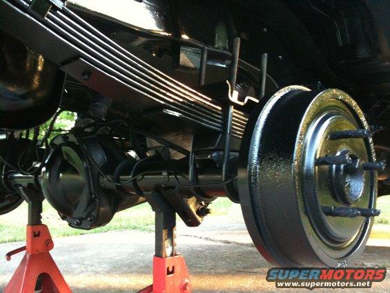 Rear axle assembly with leaf springs and brake drum, vehicle supported by red jack stands