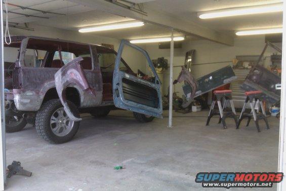 SUV body in a garage, stripped down and in primer, with doors removed