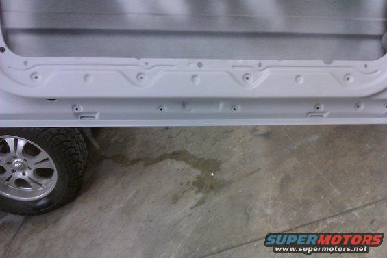 Gray vehicle door frame with visible mounting holes and a portion of a tire with a silver alloy wheel