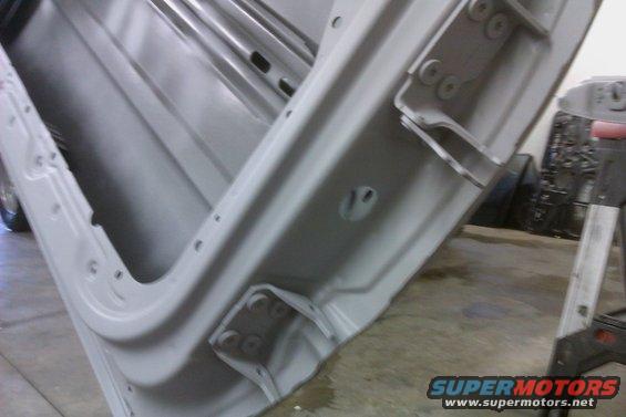 Interior view of a car door frame, showing hinges and mounting points. The metal is painted gray