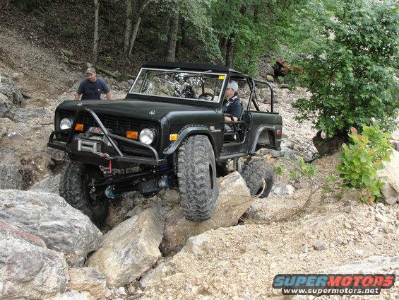 Black Ford Bronco with off-road modifications navigating a rocky trail. Driver and passenger are visible