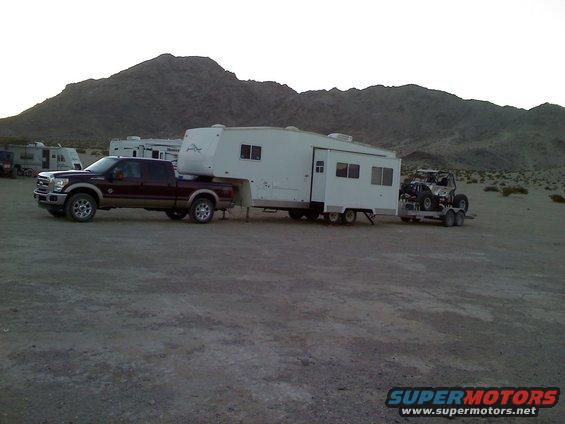Ford F-250 towing a fifth-wheel trailer with a UTV on a trailer behind it in a desert landscape