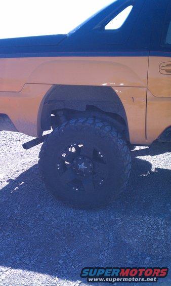 Yellow SUV side view, black roof, large off-road tire with star center cap, gravel ground