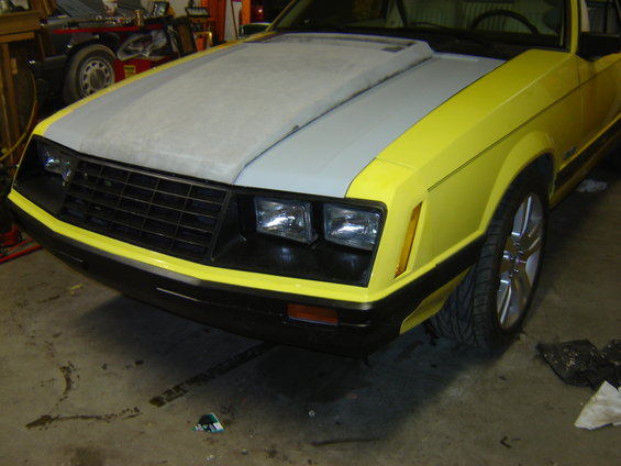 1979 Ford Mustang front end with primer gray hood and yellow fenders, parked indoors