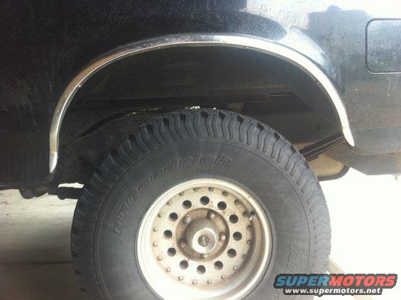 Close-up of a vehicle's rear tire and wheel well, showing a BFGoodrich tire and chrome trim around the wheel opening