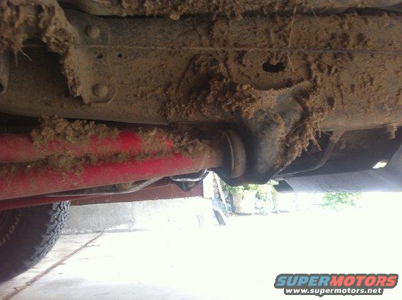 Undercarriage of a vehicle covered in mud, showing red suspension components