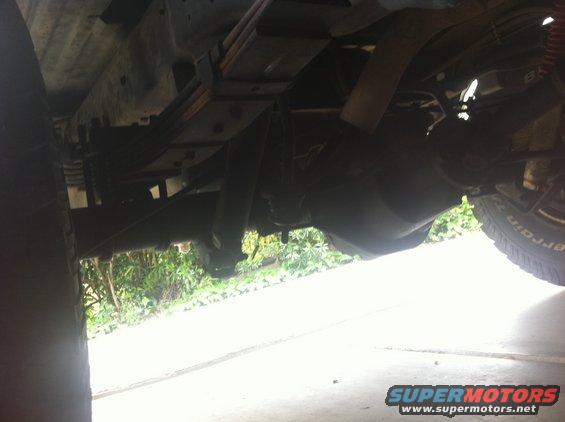 Undercarriage of a lifted truck showing leaf springs, shock absorber, and tire with 'All Terrain' text