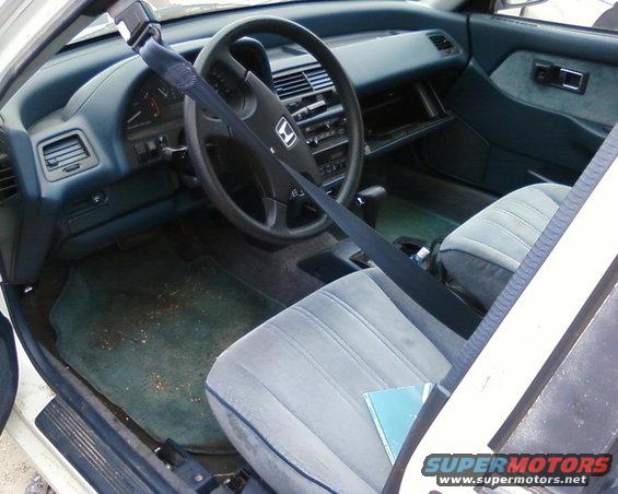 car interior with gray seats, dashboard, and steering wheel. Seatbelt is across the driver's seat