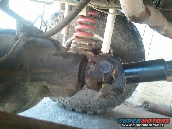 Close-up of a vehicle's rear driveshaft and differential assembly, showing the U-joint and part of the axle
