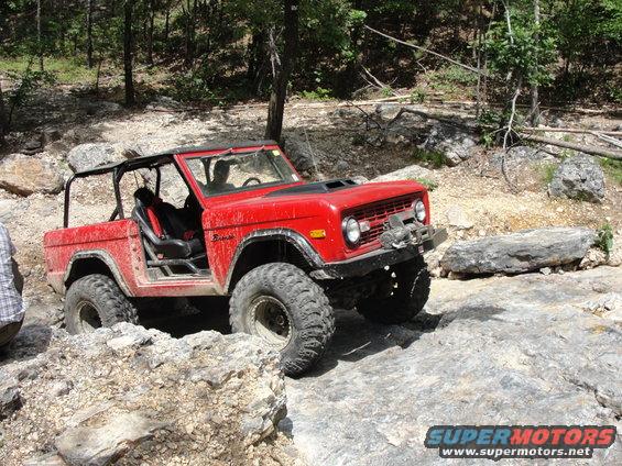 Red off-road SUV with roll cage and winch navigating rocky terrain