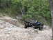 1967 Ford Mustang - Black Ford Bronco navigates a challenging rocky trail in a wooded area.