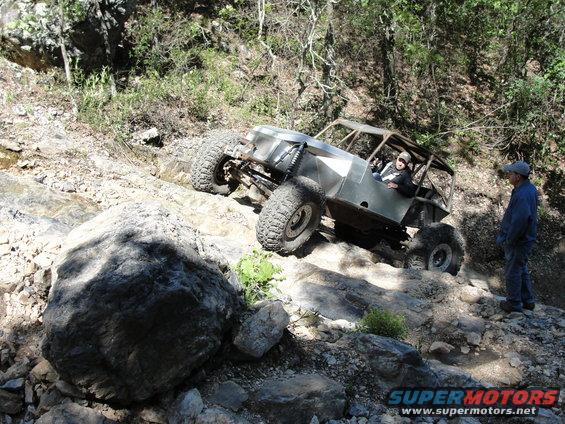 Off-road buggy with large tires climbing a rocky incline, person watching