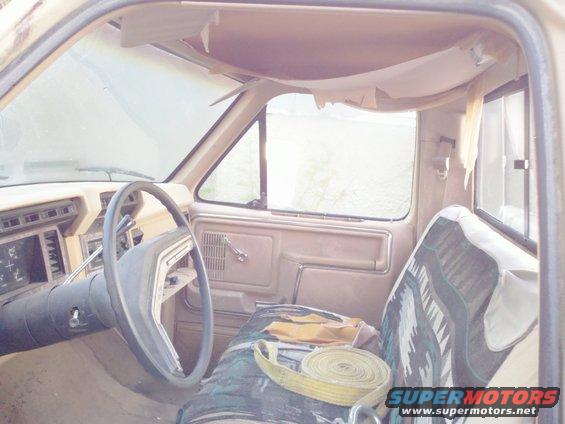 Interior of a tan 1985 Ford F-250 pickup truck, showing dashboard, steering wheel, and patterned seat cover