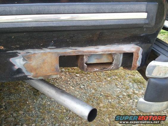 Close-up of rusty trailer hitch receiver on a vehicle's rear bumper. Exhaust pipe visible