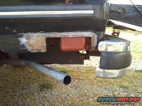 Rear bumper area of a vehicle, showing rust and repair work, with an exhaust pipe visible