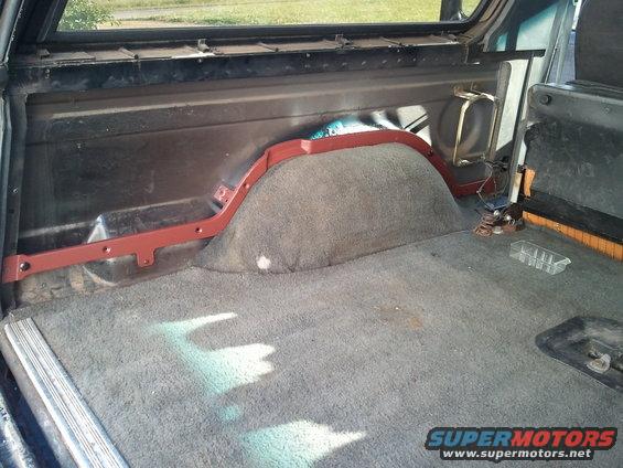 Interior cargo area of a dark-colored SUV with grey carpet and a red-painted wheel well cover