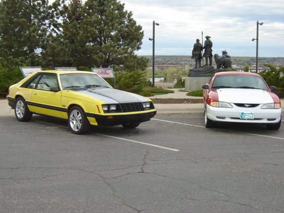 Yellow 1979 Ford Mustang coupe with grey hood parked next to a red and white car
