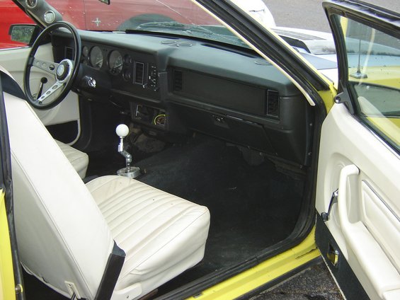Yellow 1979 Ford Mustang interior with white seats, aftermarket steering wheel, and floor shifter