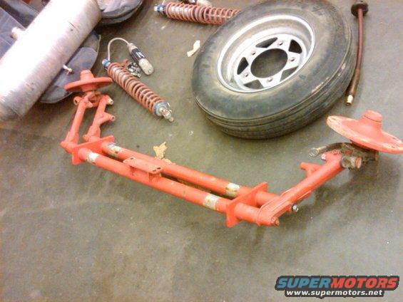 Orange painted vehicle suspension parts and a tire on a concrete floor