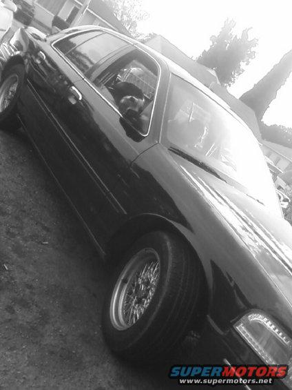 Black sedan, possibly a Ford Crown Victoria, with wire wheels. A dog is visible in the driver's seat