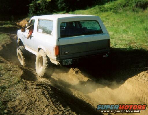 1987 Ford Bronco driving on dirt track, kicking up dust. License plate reads TON974