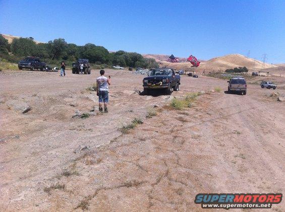 1990 Ford Bronco parked in a dirt lot with other vehicles and people