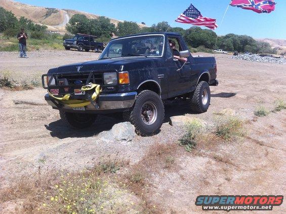 Black 1990 Ford Bronco with flags on a dirt road