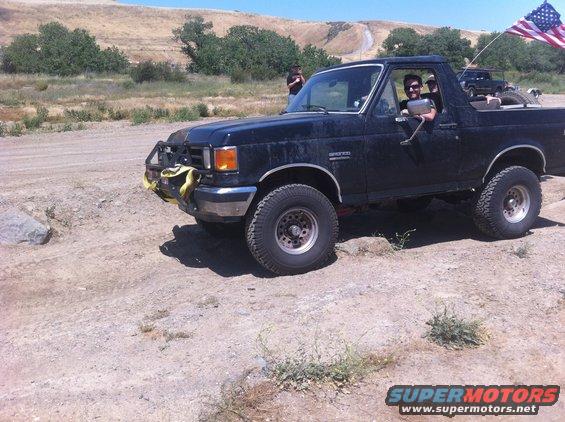 Black Ford Bronco with off-road bumper and yellow straps, driving on a dirt road