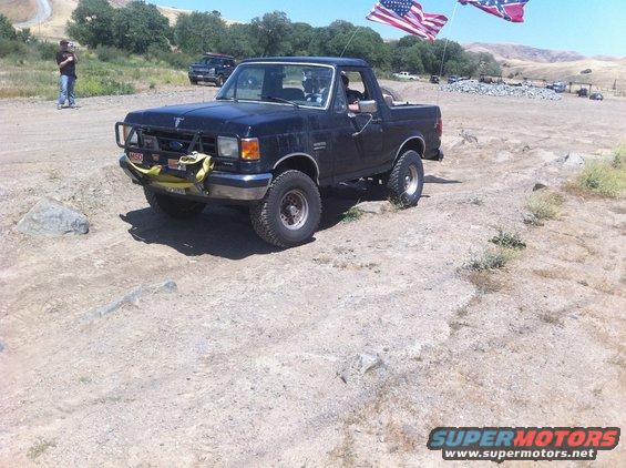 1990 Ford Bronco with bull bar and winch, parked on dirt with American and Confederate flags flying