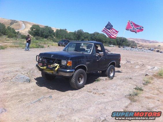 Black Ford Bronco parked on dirt road, American and Confederate flags flying from poles on the back