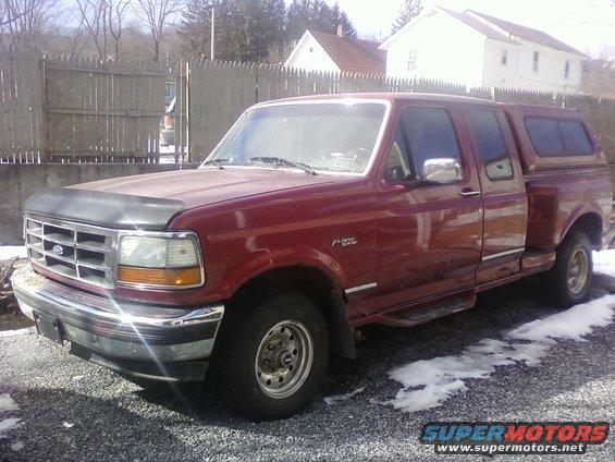 Red 1994 Ford F-150 pickup truck with a camper shell parked on gravel